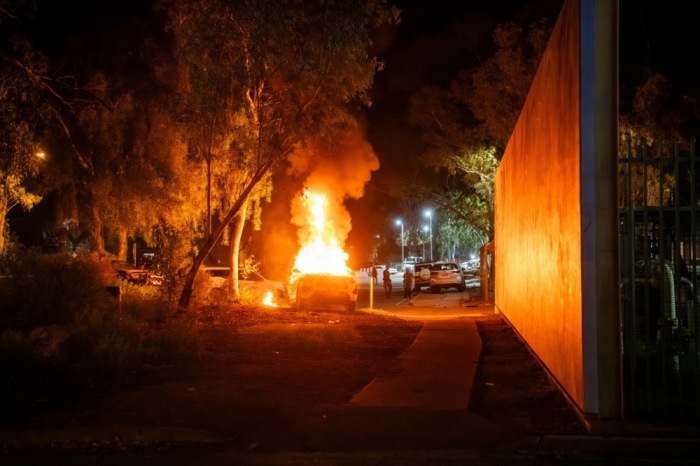 Ein Polizeifahrzeug brennt bei Ausschreitungen vor einem Krankenhaus in Alice Springs nach Festnahme eines Verdächtigen im Fall eines getöteten Kindes. Foto: EPA/Rhett Hammerton