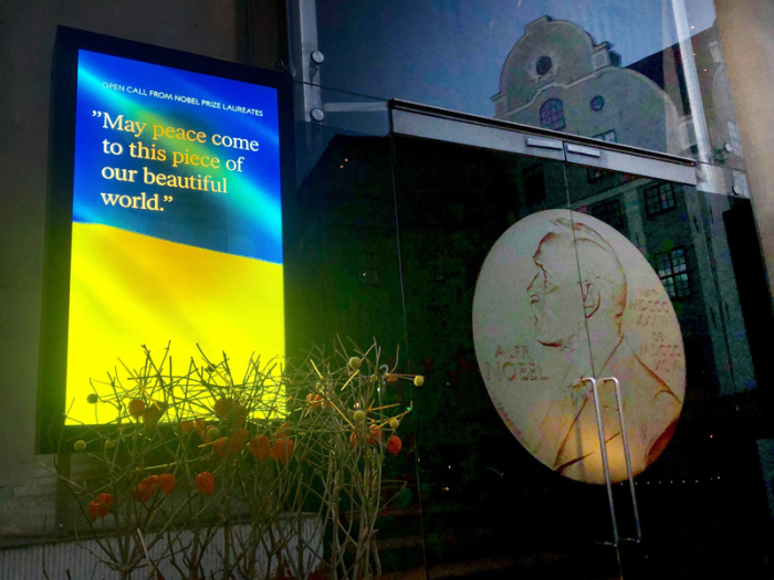 Auf einem Bildschirm vor dem Nobelpreismuseum in Stockholm ist eine Ukraine-Flagge zu sehen mit dem Schriftzug 