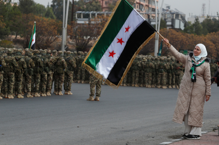 Bei Feiern in Damaskus schwenkt eine Frau die syrische Flagge, während Soldaten der neuen Armee ein Jahr nach Assads Sturz Aufstellung nehmen. Foto: dpa/Omar Sanadiki