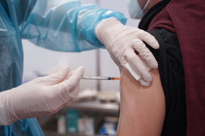 Ein junger Mann wird mit einer Booster-Dosis eines Corona-Impfstoffs im Impfzentrum in der Schinkelhalle gegen das Coronavirus geimpft. Foto: Jörg Carstensen/dpa