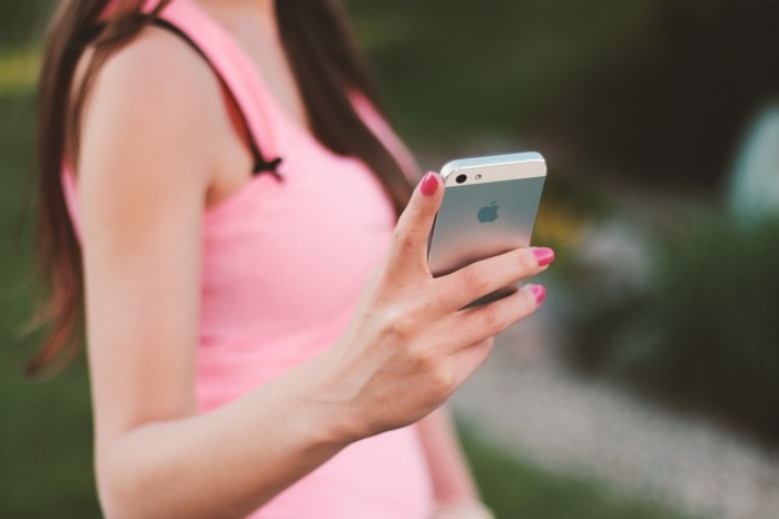 Eine Frau in einem pinken Top hält ein Smartphone in der Hand, eine Darstellung der mobilen Vernetzung in der heutigen Gesellschaft. Foto: Pixabay/Jan Vašek