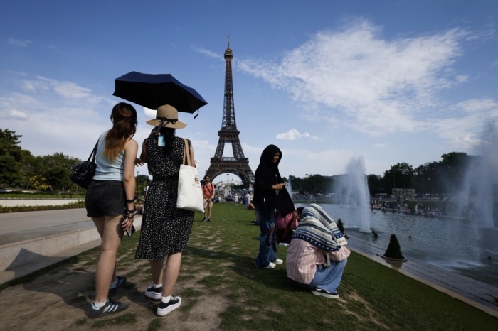 Frauen suchen unter einem Sonnenschirm am Trocadéro-Brunnen am Eiffelturm in Paris Schutz vor der Hitze. Foto: epa/Yoan Valat