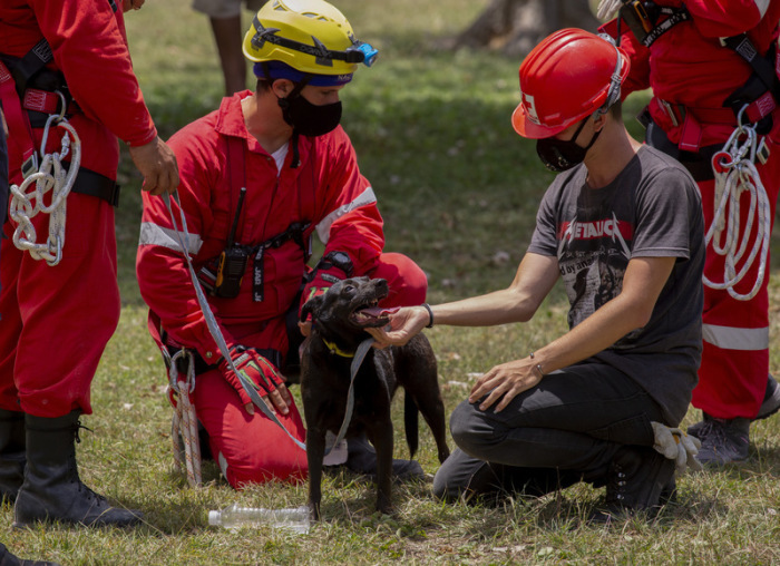 08.05.2022, Kuba, Havana: Mitglieder des Roten Kreuzes spielen mit einem Hund, der aus den Trümmern des explodierten Fünf-Sterne-Hotels Saratoga gerettet wurde. Foto: Ismael Francisco/Ap/dpa