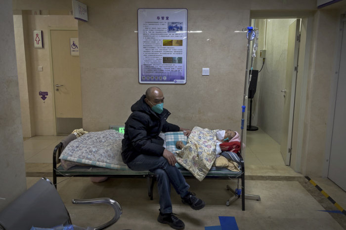 Ein Mann mit Mund-Nasen-Schutz kümmert sich um seinen älteren Verwandten, der in einem Korridor der Notaufnahme eines Krankenhauses intravenöse Infusionen erhält. Foto: Andy Wong/Ap/dpa