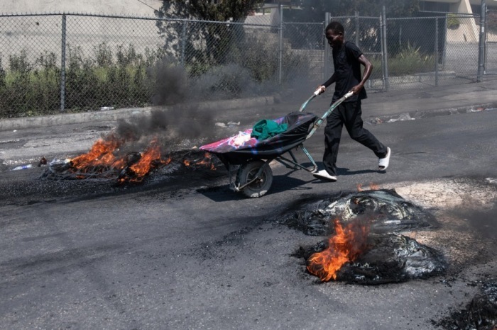 Ein Mann schiebt einen Wagen an Reifen vorbei, die von Demonstranten während einer Demonstration in Port-au-Prince in Brand gesetzt wurden. Foto: epa/Johnson Sabin