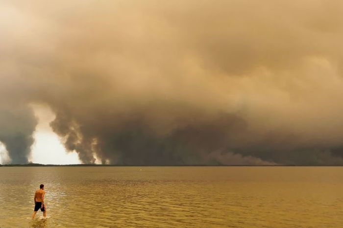 Ein Strandbesucher spaziert am Strand von Moutchic in Lacanau, während Rauchwolken eines Waldbrands aufsteigen. Foto: dpa/Maximilien Lamy