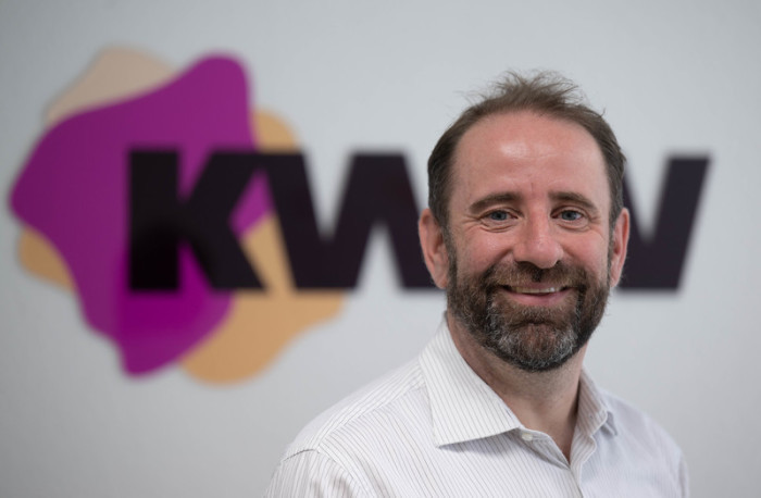 Robert Brückmann, Leiter des Kompetenzzentrums Kommunale Wärmewende, vor dem Logo der Einrichtung in Halle. Das Zentrum unterstützt Städte und Gemeinden bei der Wärmeplanung. Foto: Hendrik Schmidt/dpa.