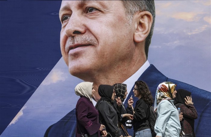 Women walk in front of an election campaign poster of Turkish President Recep Tayyip Erdogan, in Istanbul,