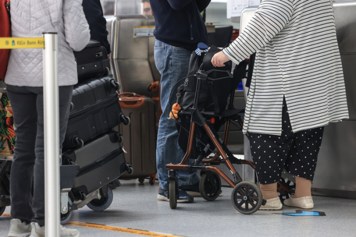 Eine Frau mit Rollator steht im Flughafen-Terminal am Check-In-Schalter. Flughäfen müssen sich stärker auf die Bedürfnisse älterer Reisender einstellen. Foto: Oliver Berg/dpa
