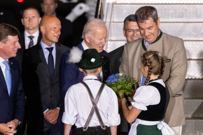 Die Kinder Daniela Hauser und Marco Keller begrüßen Joe Biden (M), Präsident der USA, mit einem Blumenstrauß bei seiner Ankunft am Flughafen München. Daneben steht Markus Söder (r, CSU), Ministerpräsident von Bayern. D... Foto: Daniel Karmann/dpa
