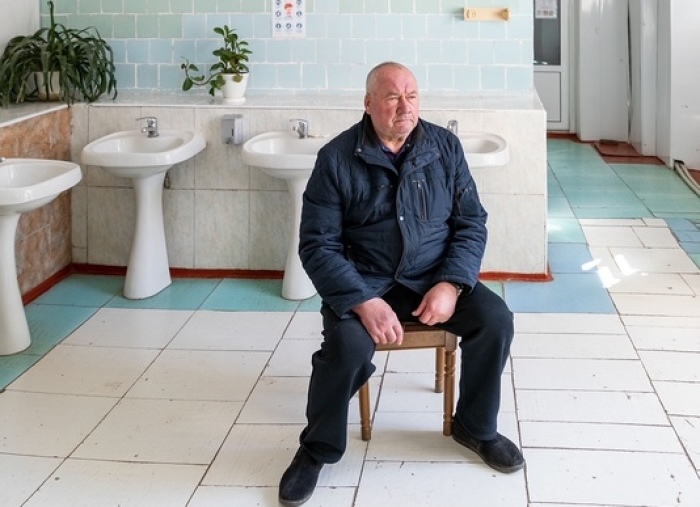 Wladimir Getmantschuk, Direktor einer Sonderschule sitzt in einem Waschraum unter einer Installation des Künstlers Aljoscha. Foto: Aljoscha Potupin/dpa