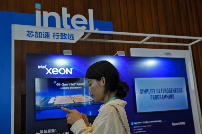 Eine Frau schaut auf ihr Smartphone in der Nähe eines Intel-Standes, der für Xeon-Chips wirbt. Foto: Andy Wong/Ap/dpa