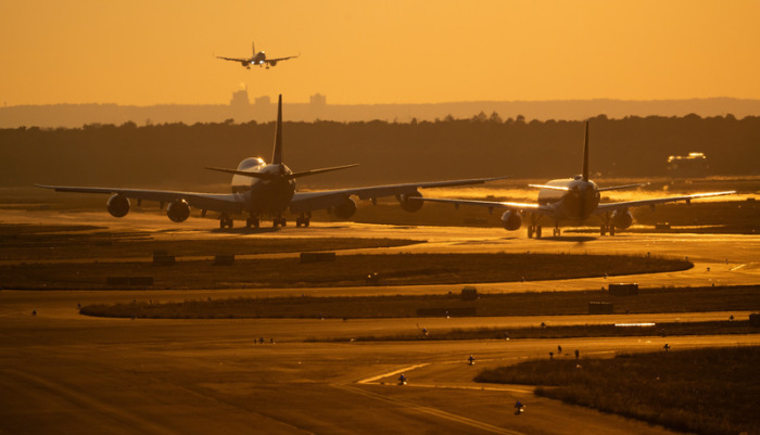 Flugzeuge rollen im Licht der untergehenden Sonne zu ihrer Parkposition auf dem Flughafen Frankfurt, während eine weitere Maschine zur Landung ansetzt. Foto: Boris Roessler/dpa