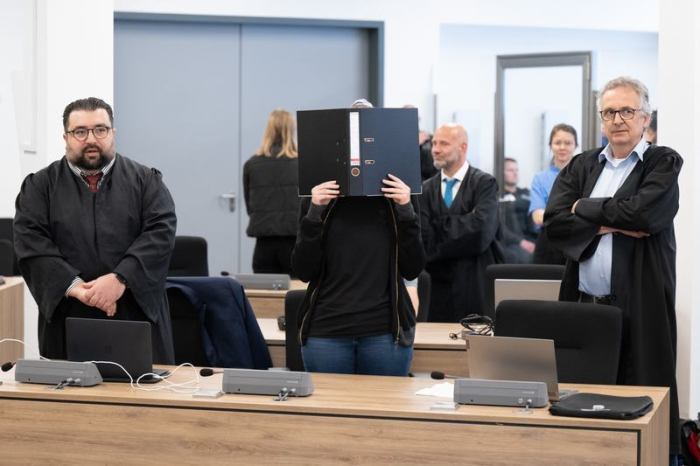 Die Angeklagte (M) steht bei der Fortsetzung des Prozesses im Oberlandesgericht (OLG) Dresden im Verhandlungssaal und hält einen Aktenordner vor ihr Gesicht. Foto: Sebastian Kahnert/dpa