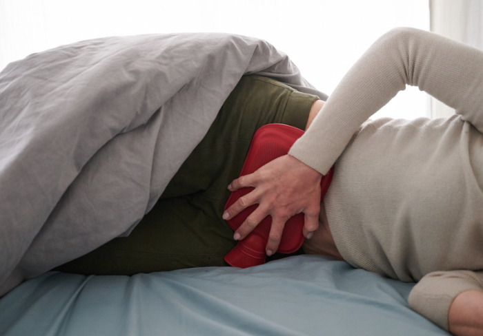 Eine Frau hält sich eine Wärmflasche an den Unterbauch, während sie im Bett liegt (gestellte Szene). Foto: Annette Riedl/dpa