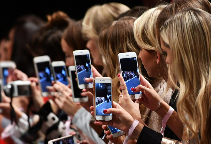 Frauen mit Smartphones filmen und fotografieren bei einer Show des Labels Marc Cain bei der Fashion Week. Foto: Jens Kalaene/dpa