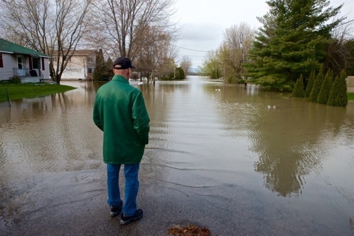 Ein evakuierter Mann steht vor überfluteter Straße, nachdem schwere Regenfälle zahlreiche Häuser und Gemeinden in Quebec getroffen haben. Foto: epa/Andre Pichette