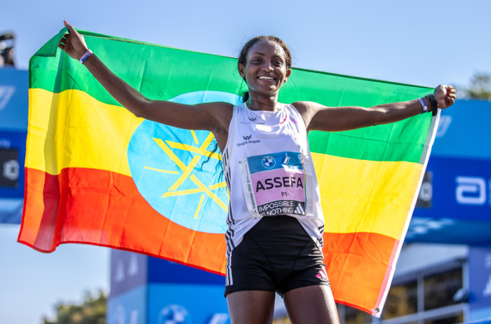 Tigst Assefa aus Äthiopien jubelt mit einer Fahne, nachdem sie beim Berlin Marathon nach 2:11:53 Stunden als erste Frau durchs Ziel lief und damit einen Weltrekord erreichte. Foto: Andreas Gora/dpa