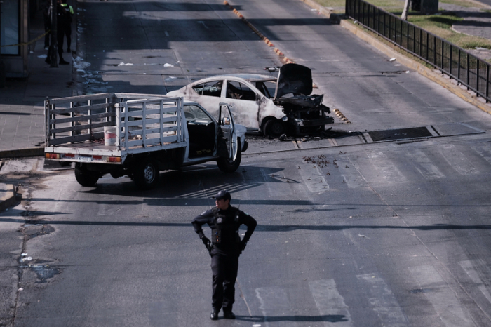 Ein Polizist sichert eine Straße in Guadalajara, nachdem brennende Fahrzeuge in mehreren Bundesstaaten aus Protest und Gewalt den Verkehr blockieren. Foto: Alejandra Leyva/Ap/dpa