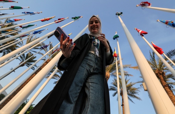 Eine Frau macht ein Selfie neben Flaggen während der COP28-Konferenz in Dubai. Foto: EPA-EFE/Ali Haider