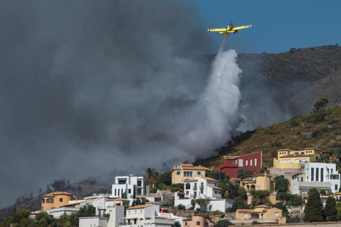 Ein Löschflugzeug verteilt Wasser auf die Flammen neben mehreren Häusern in der Gegend von Atzubia, Alicante. Foto: epa/Natxo Frances