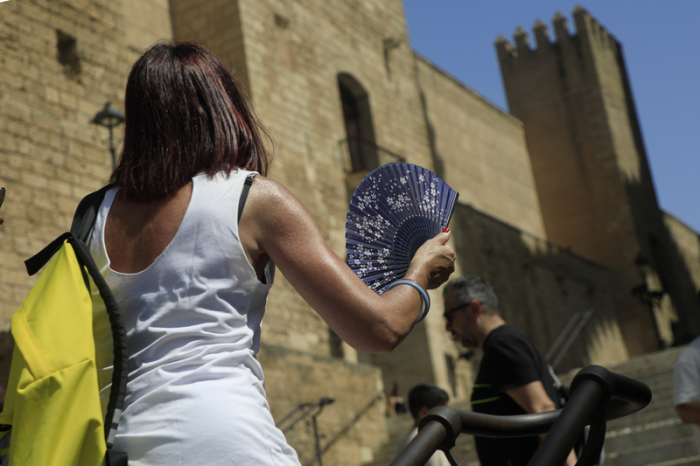 Eine Frau mit einem Fächer geht während einer Hitzewelle in der Innenstadt von Palma spazieren. Foto: Clara Margais/dpa