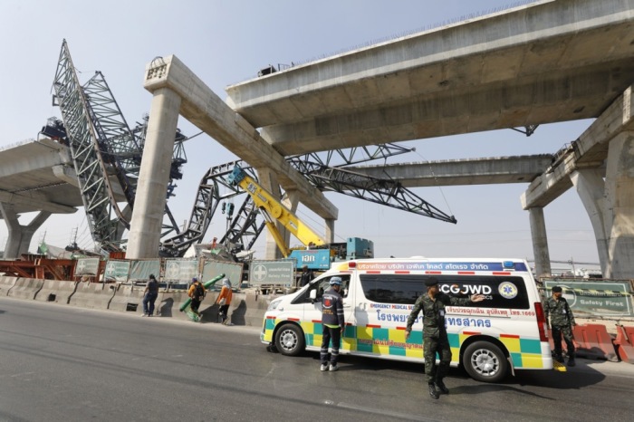 Rettungskräfte und Sicherheitskräfte stehen an der Unglücksstelle in Samut Sakhon, nachdem ein Baukran auf eine Schnellstraße gestürzt ist. Zwei Menschen kamen ums Leben, mehrere wurden verletzt. Foto: epa/Narong Sangnak